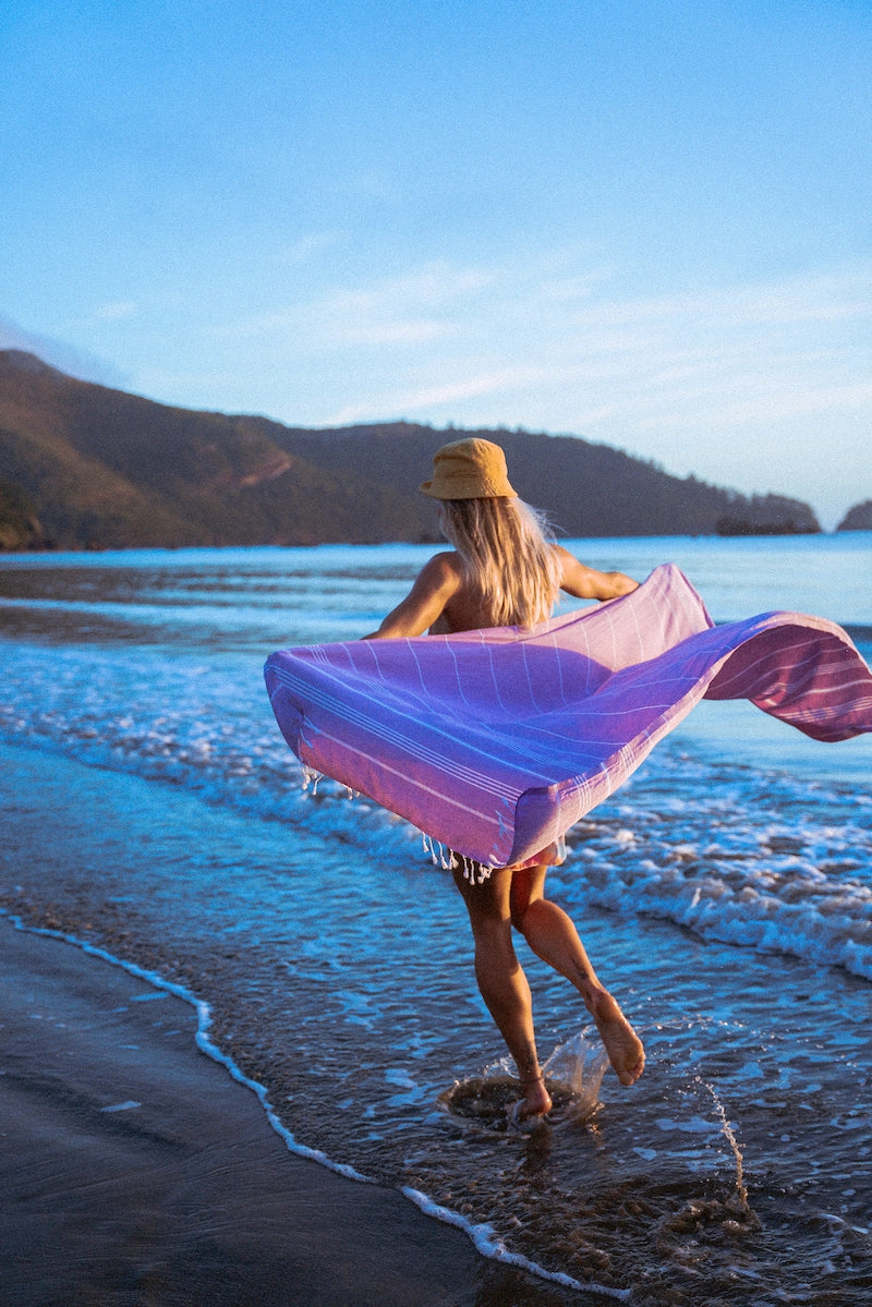 A purple Wetcat Turkish towel is held by a traveler like a cape in an exotic location while she's running